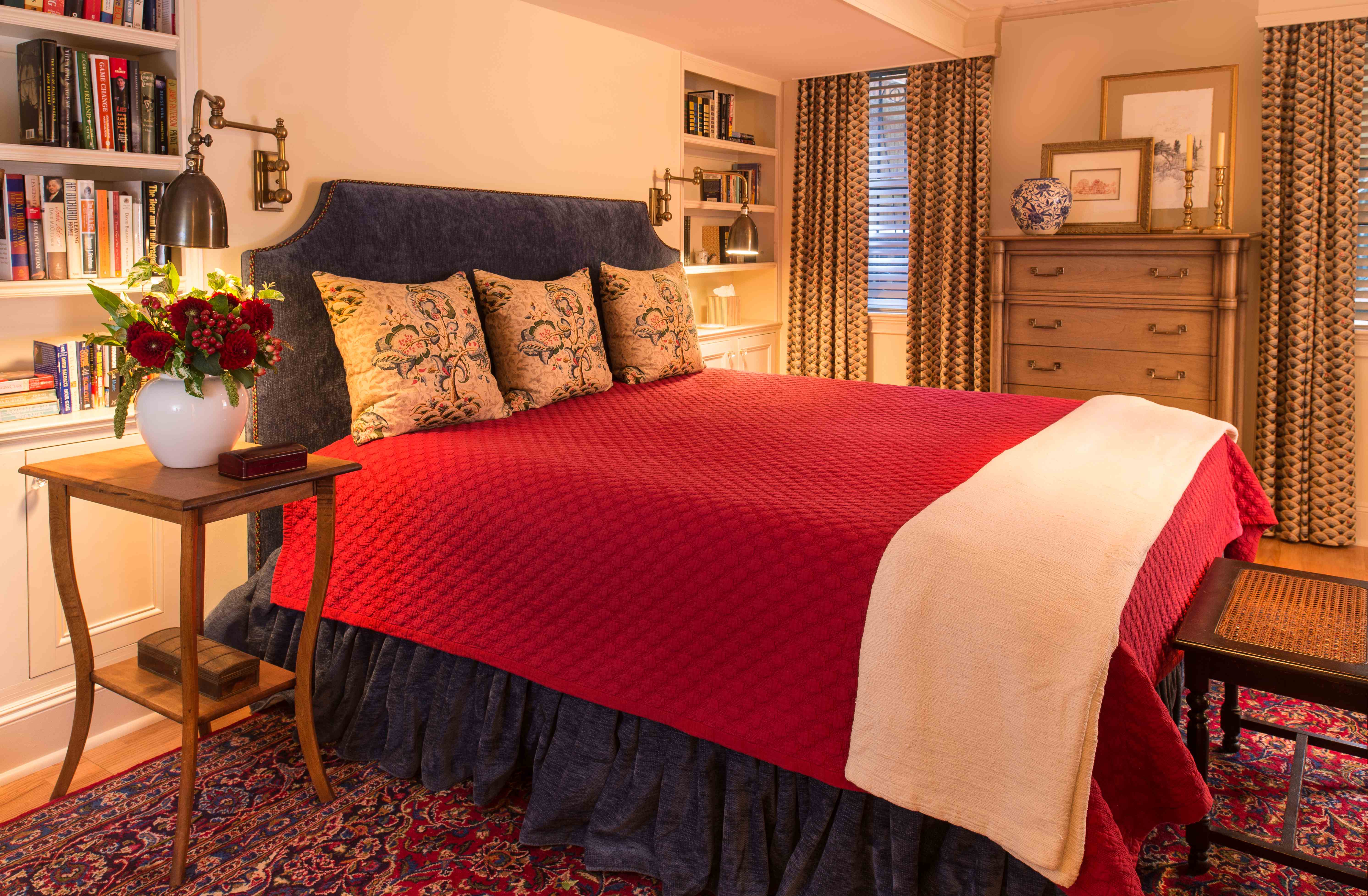 This traditional bedroom design by Elizabeth Swartz Interiors of Boston gets romantic without being too feminine by utilizing soft and luxurious textiles in rich jewel tones and reds, as well as big throw pillows, soft lighting and fresh flowers.